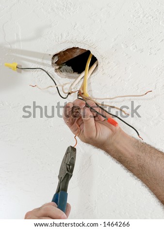 A closeup of an electrician\'s hands as he uses pliers to straighten electrical wires.  Work is being performed to code by a licensed master electrician.