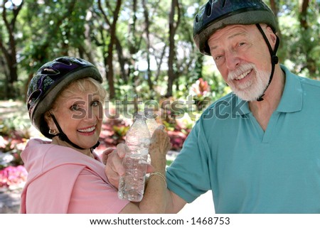 A fit senior couple cooling off with water after riding their bikes.
