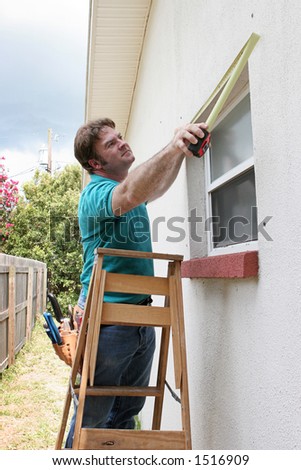 A carpenter or handyman measuring windows for storm shutters.