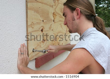 stock photo A young man screwing plywood over a window on his home in 