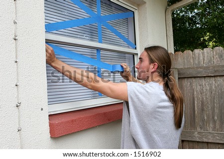 A young man taping windows on his home in preparation for a hurricane.