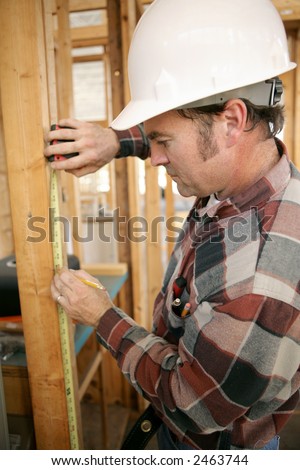 A vertical view of a construction worker measuring a wood beam on a construction site. Focus on his face.