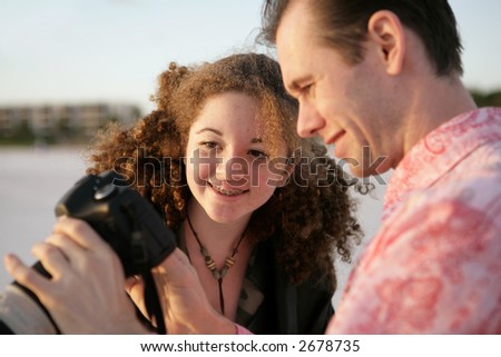 A photographer showing his photos to a friend.  Focus is on the girl and her reaction. Warm late afternoon sun.