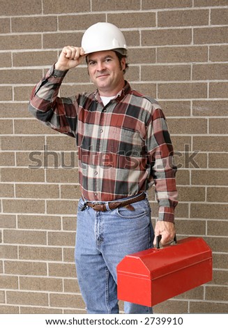 A handsome construction worker carrying his toolbox and tipping his hard hat.