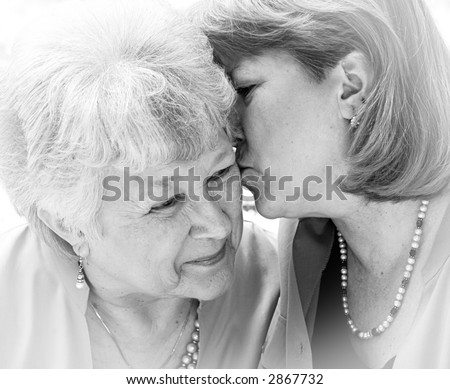 An adult woman kissing her senior mother.  Black and white with vignette.