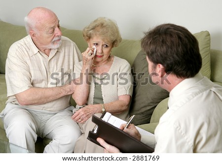 A senior couple in counseling - either grief counseling or marriage counseling.  The wife is crying and the husband is wiping her tears and trying to console her.