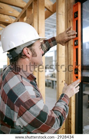 A construction worker checking that a newly installed window is level.  Vertical view.  Authentic and accurate content.