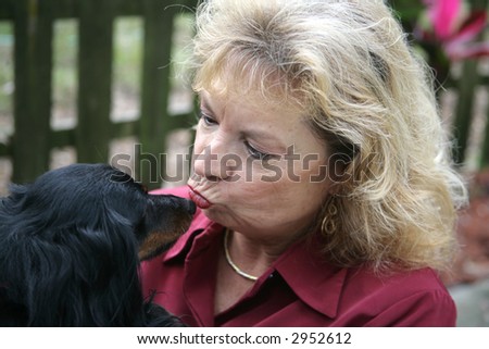 A woman kissing her long haired dachshund on the nose.