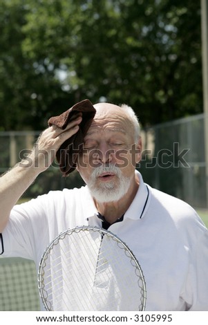 A hot and tired senior man wiping his brow after a tennis match.