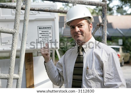A building inspector standing under scaffolding pointing out the WARNING sign posted on the job-site.