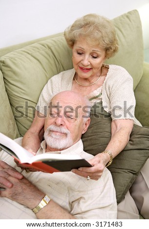 A senior couple reading together.  The wife is reading to the husband.