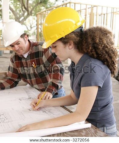 A female engineering student on a construction site marking blueprints as her instructor watches.