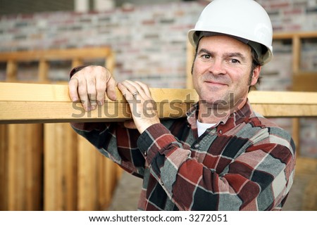 A friendly appealing construction worker in classic pose, carrying planks on the jobsite.  Model is actual construction worker. Authentic and accurate content depiction.