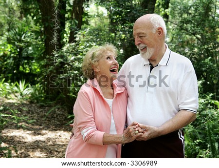 A happy, active senior couple laughing together on a walk through the park.  She's wearing a hearing aid.  Plenty of copy space.
