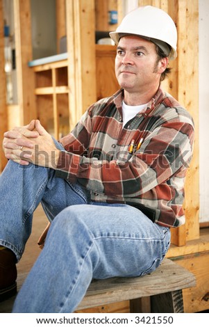 A tired construction worker sitting down resting at the end of the day.  Authentic construction worker on actual job site.