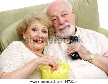A happy senior couple with the remote control and the popcorn, ready to watch television.