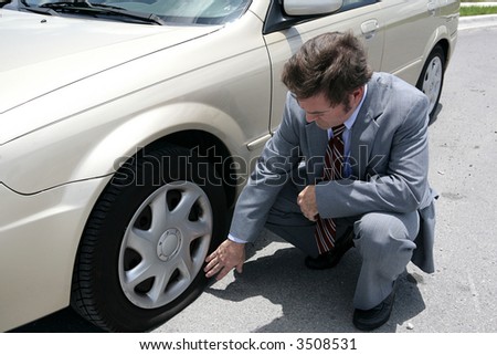 A man dressed for a business meeting discovering a flat tire on his car.