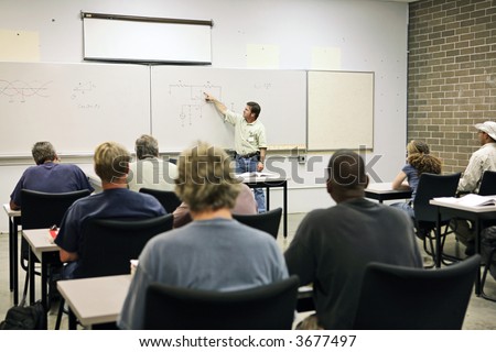 An adult education teacher pointing to an electrical circuit on the board.  Focus on the diagram of the circuit.