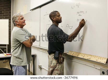 A vocational education teacher looking on as a student does equations on the board.