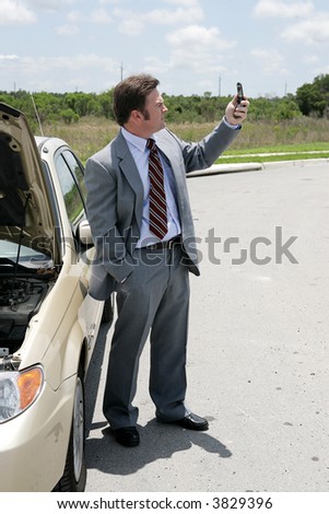 A businessman whose care has broken down in a remote location checking for phone signal.