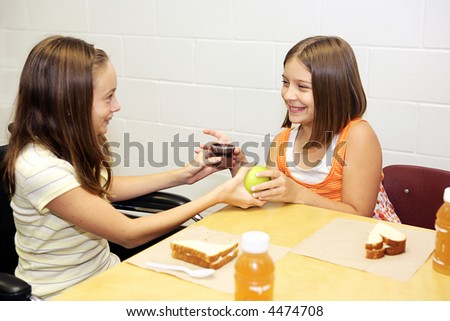 Two school girls at lunch trading desserts - an apple for pudding.