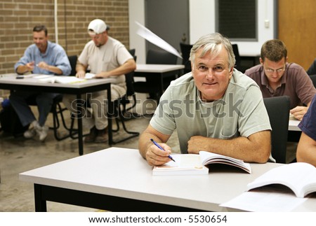 An older adult education student takes school seriously while the younger guys are goofing off making paper airplanes.