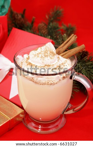 Christmas eggnog in a mug with whipped cream, a sprinkling of nutmeg, and cinnamon sticks.  Photographed on a red background surrounded by gifts.