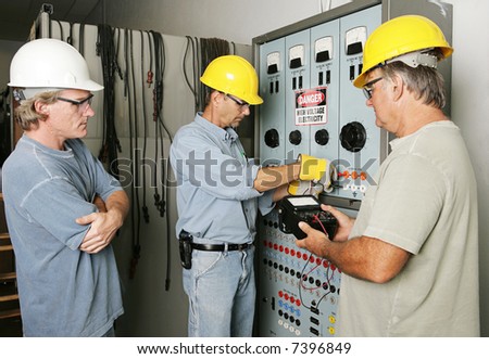 Electricians working on an industrial power distribution center while supervisor watches.  All work being performed according with industry code and safety standards.