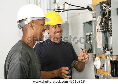 Two electricians working on an electrical panel together.  Actual electricians performing work according to industry code and safety standards.