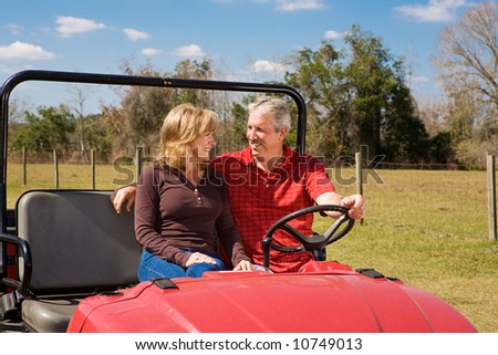 Good looking retired couple riding an all terrain vehicle through a rural landscape.  Wide view with plenty of room for text.