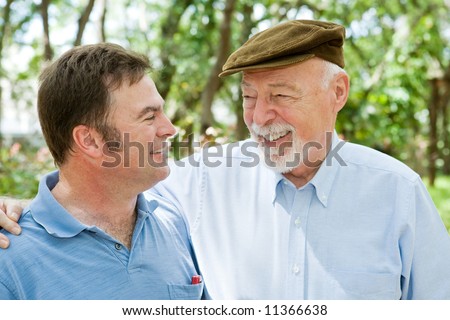 Senior father and adult son laughing together in the park.