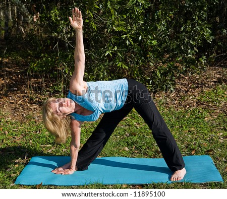 Beautiful, fit woman in her sixties doing the triangle yoga asana, outdoors in a natural setting.