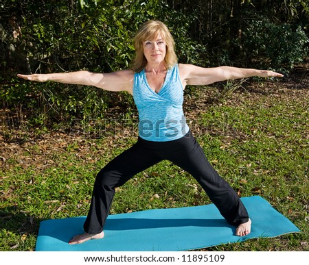 Fit beautiful sixty year old woman doing the warrior pose in yoga in a natural setting.