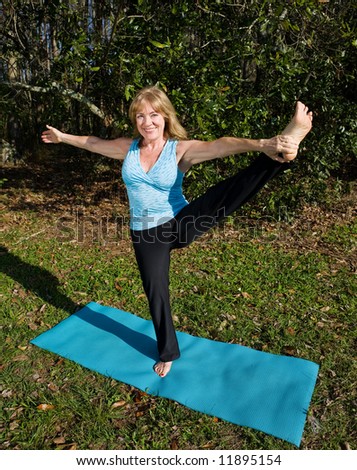 Amazingly limber sixty year old woman doing a yoga stretch standing on one leg.