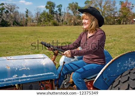 Beautiful mature woman driving a tractor on the farm.