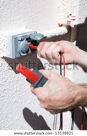 Closeup of an electricians hands using a voltage meter on an electrical receptacle.  Model is an actual electrician.  All work is being performed according to industry code and safety standards.