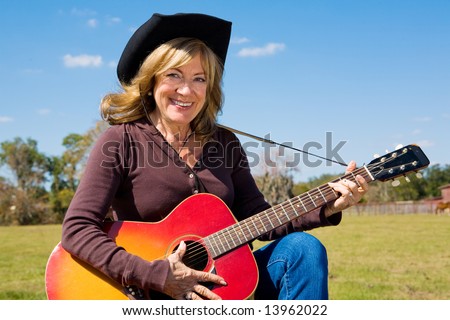 Beautiful mature cowgirl plays country music on the farm.