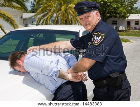 Police officer looking at camera as he arrests a suspect.
