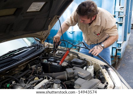 Auto mechanic using jumper cables to charge a car battery.