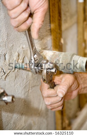 Closeup of plumbers hands using crescent wrenches to tighten a valve.  Shallow depth of field.