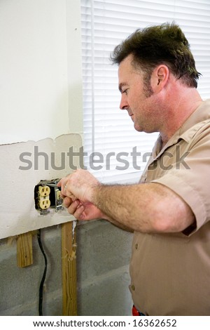 Electrician replacing an old receptacle during a kitchen remodeling job.  Model is a licensed Master Electrician  - all work being performed according to industry code and safety standards.