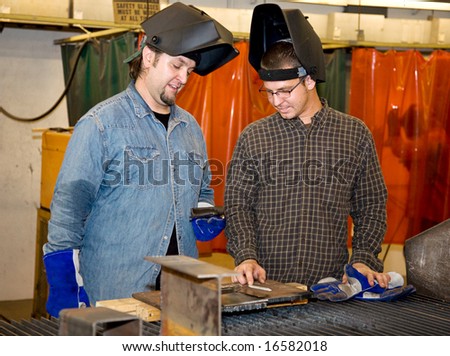 Two welders in a factory discussing how to work a piece of metal.  Authentic and accurate content depiction with all work being performed in accordance with industry code and safety regulations.