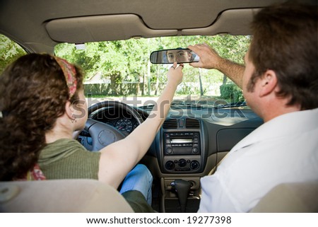 Teen girl and her driving instructor adjusting rearview mirror.  Focus on girl in the mirror.