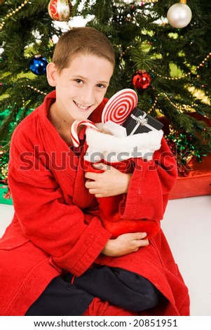 Adorable little boy under the Christmas tree, hugging his stocking.
