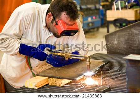 Worker using an acetylene torch to cut through metal in a metalworks factory.