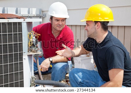 Air conditioning repairmen discussing the problem with a compressor unit.
