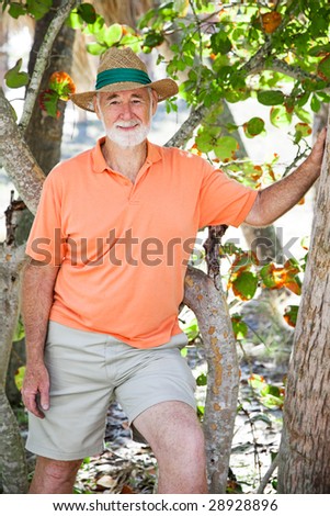 Portrait of a handsome, casually dressed senior man in a grove of trees.