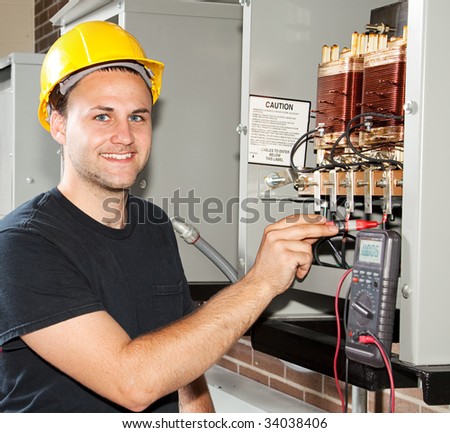 Young apprentice electrician measures power coming through coils of an industrial power distribution center.