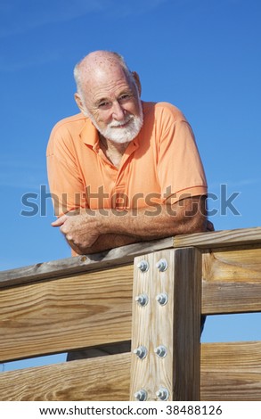Portrait of a handsome, fit senior man leaning on a wood railing.