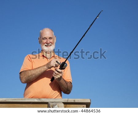 Senior man enjoys fishing off a pier, against a beautiful blue sky.